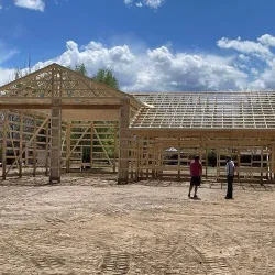 Two workers in front of a post frame building under construction